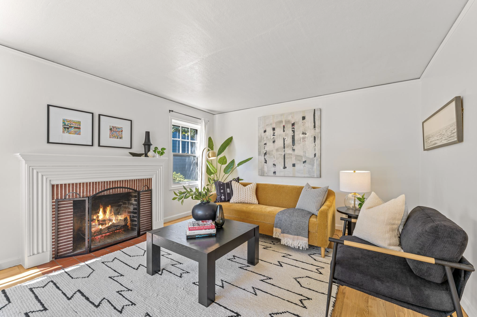 Cozy living room with a fireplace, mustard yellow sofa, black coffee table, and various framed artworks on white walls.
