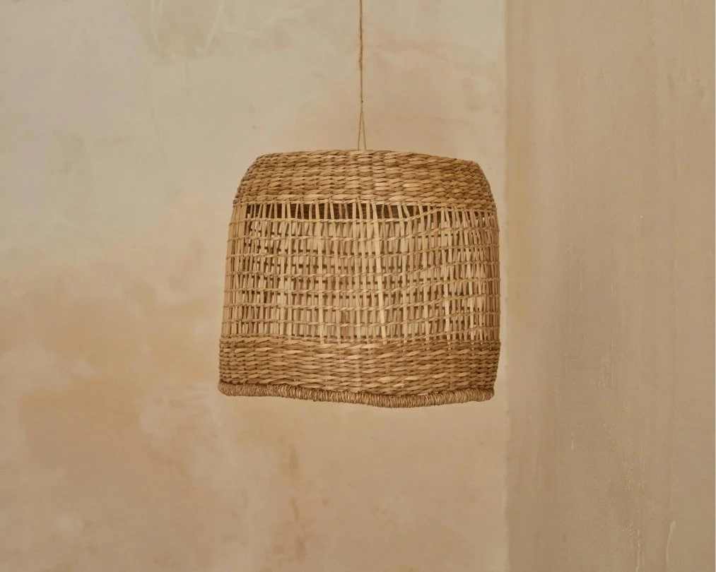 Woven wicker lampshade hanging from the ceiling against a plain beige wall.