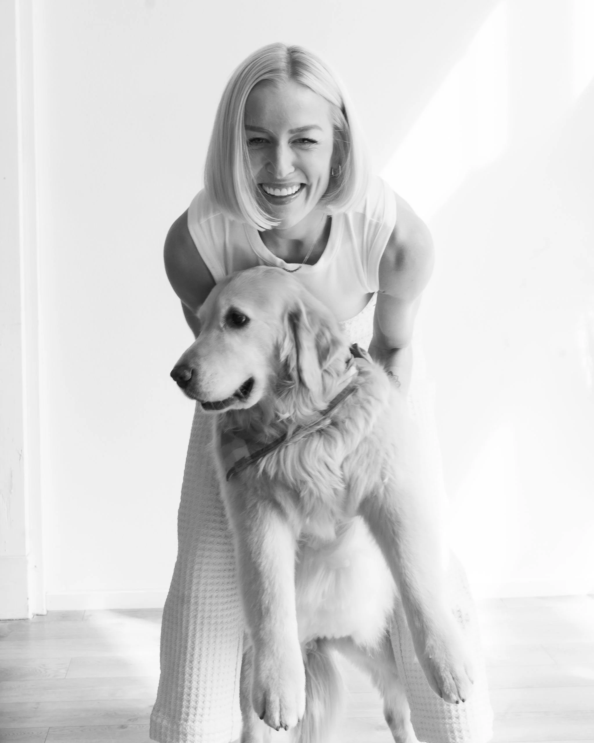 A blonde hair woman leaning forward smiling with a golden retriever for Ortega Collective Real Estate agency brand photos.