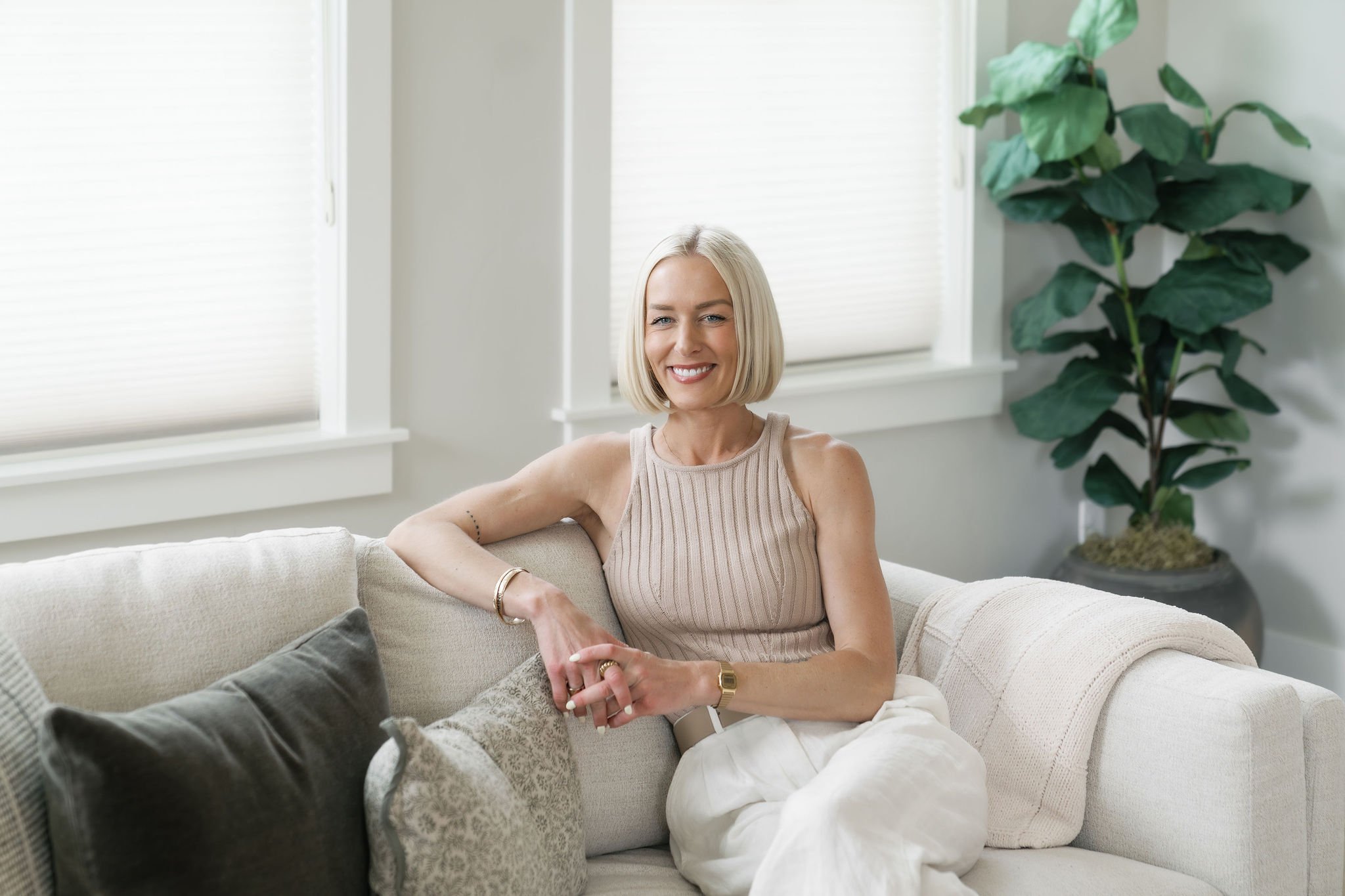 A blond woman sitting on a white couch in a bright room is Chelsea Ortega a real estate agent in Bend Oregon.