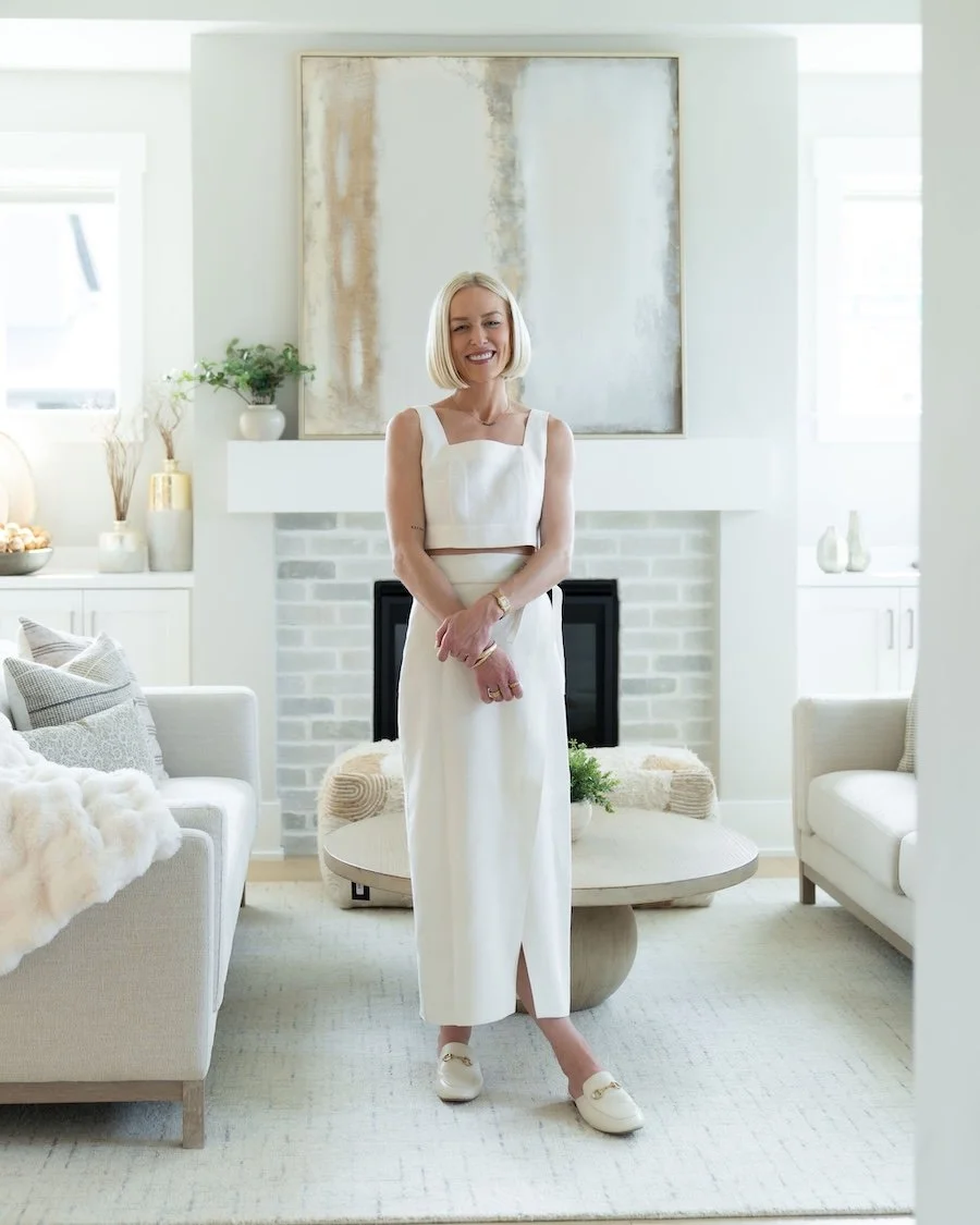 A smiling woman with blonde hair smiling in a light-colored furniture and decor is Chelsea Ortega, a Bend Real Estate Agent.