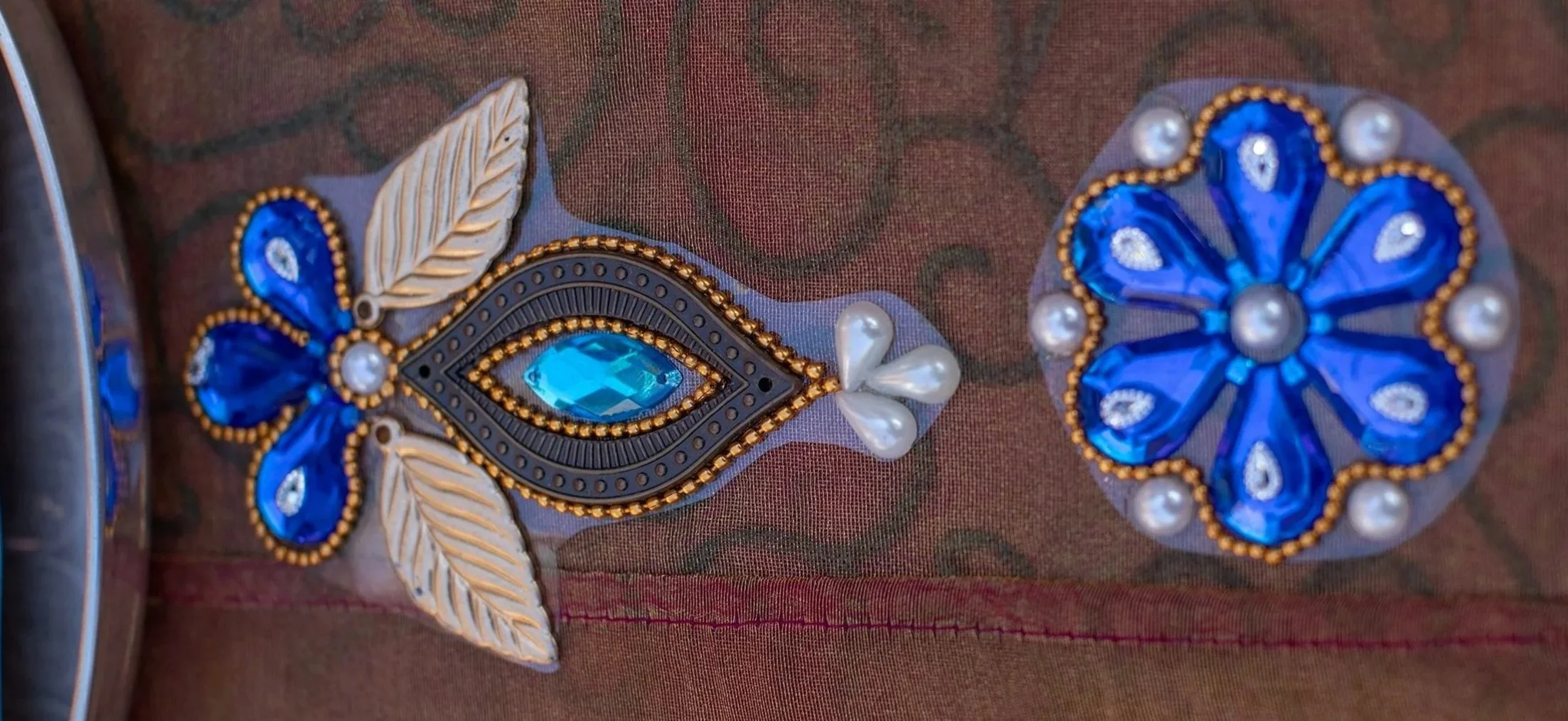 Close-up of embroidered blue and pearl decorative patches on a fabric surface.