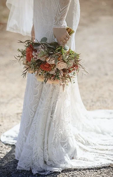 A bride in a white lace wedding dress holding a bouquet of flowers