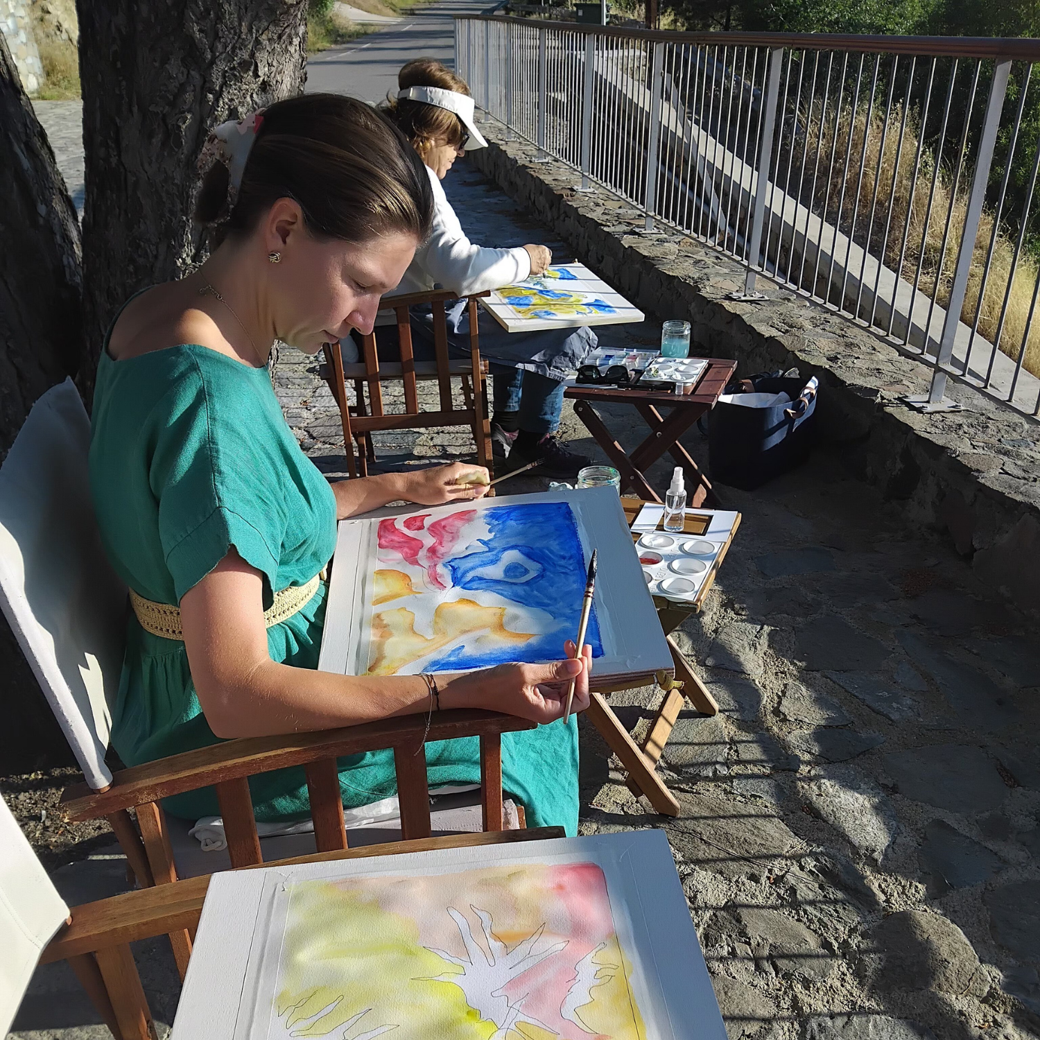 Two women sitting outdoor and painting
