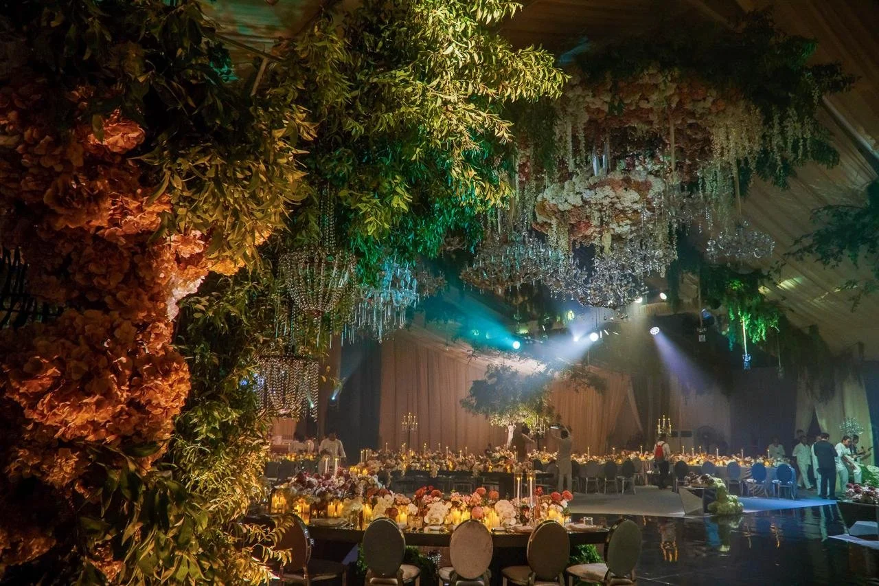 Elegant event hall decorated with floral arrangements, chandeliers, and ambient lighting, with round tables set for a formal gathering.