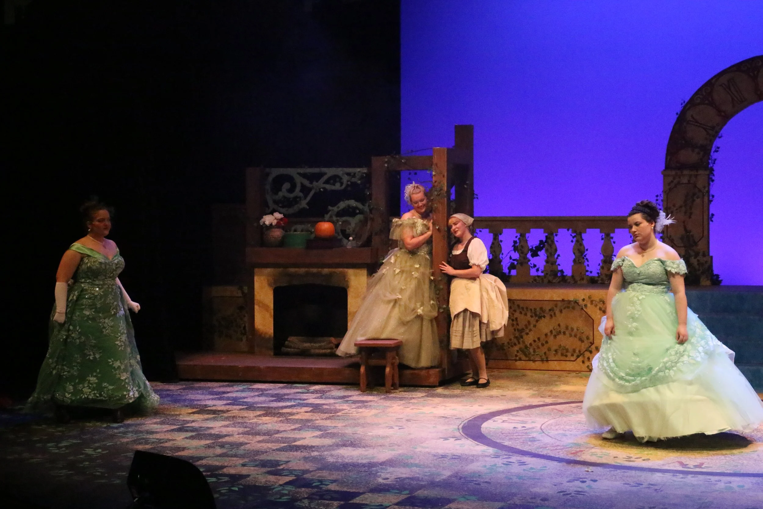 Women dressed in 18th-century costumes performing on stage with set design resembling a balcony and kitchen area.