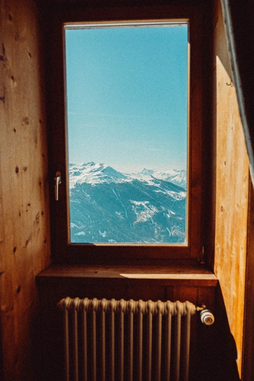 View of snow-capped mountains through a window in a wooden cabin