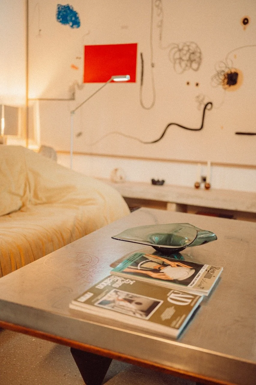 A coffee table with magazines and a green glass dish in a cozy living room with a cream-colored sofa and abstract wall art.