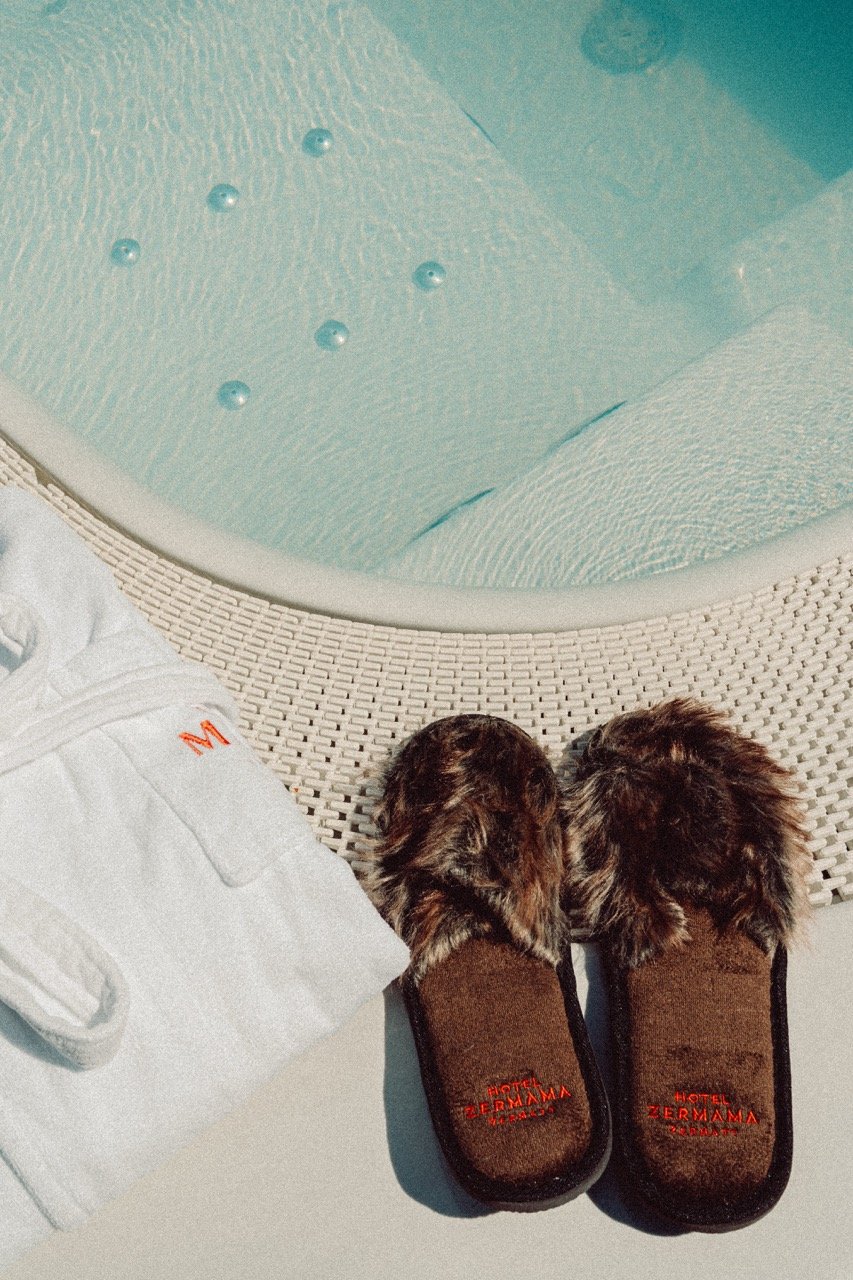 A pair of hotel slippers standing next to a hot tub in a sunny atmosphere