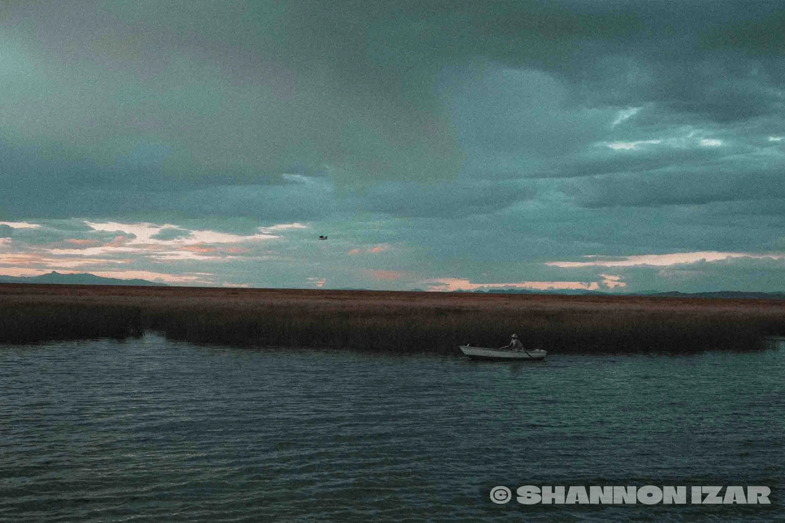 Paysage du lac Titicaca avec un bateau et des montagnes à l'horizon sous un ciel nuageux