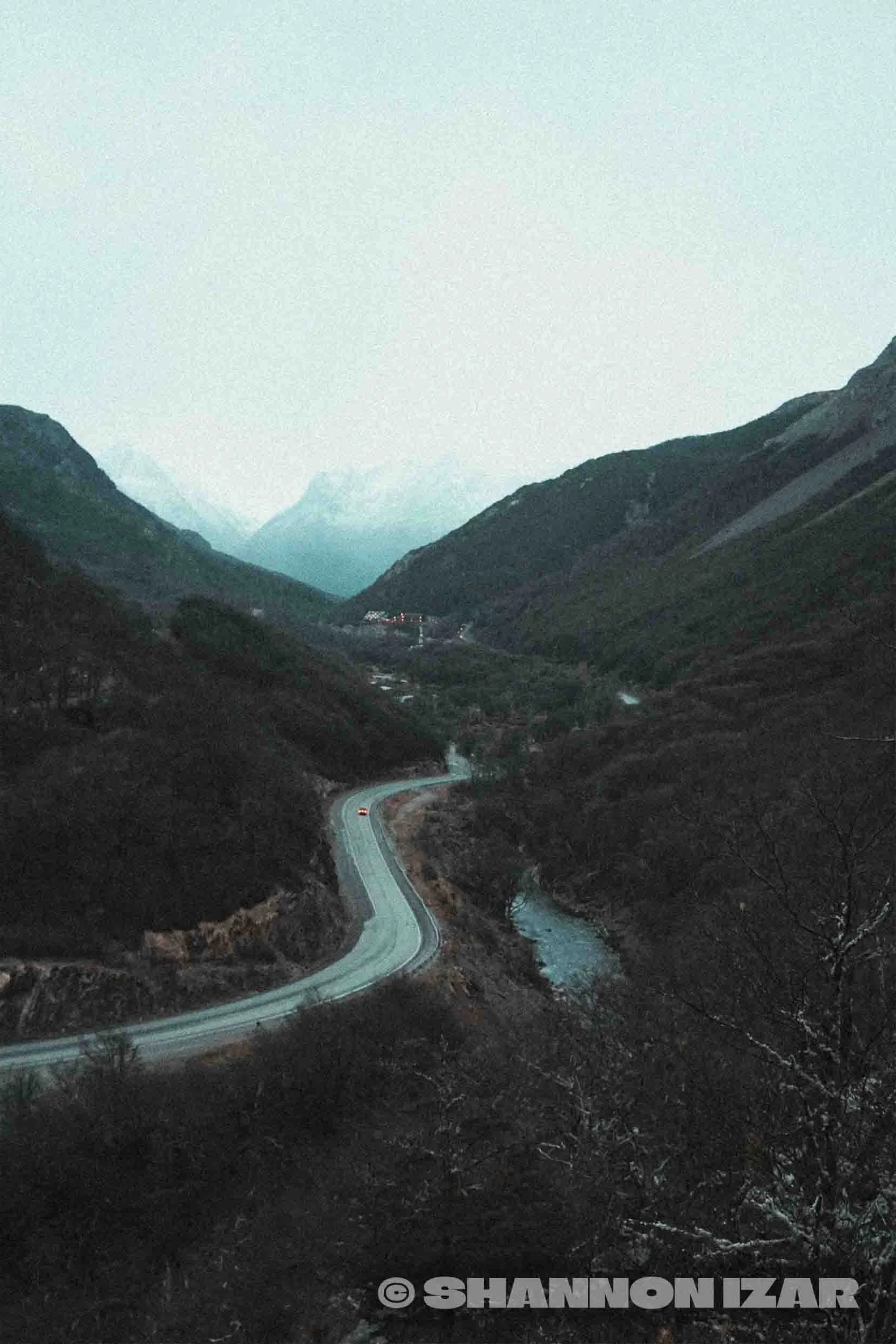 Une vallée montagneuse avec une rivière et une route sinueuse, vue depuis une altitude élevée au crépuscule.