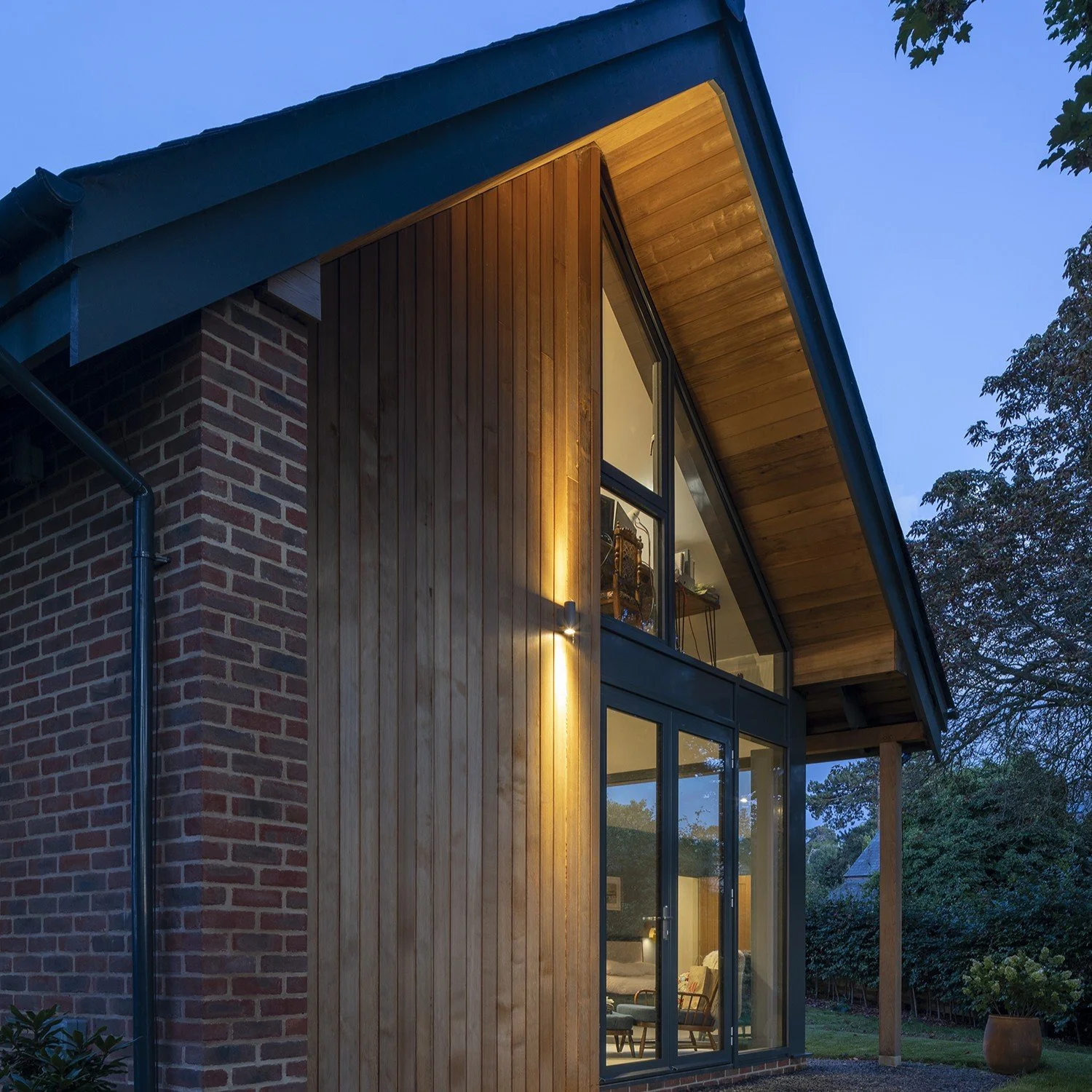 Modern house with a combination of brick and wooden exterior, large windows, and a sloped roof at dusk.