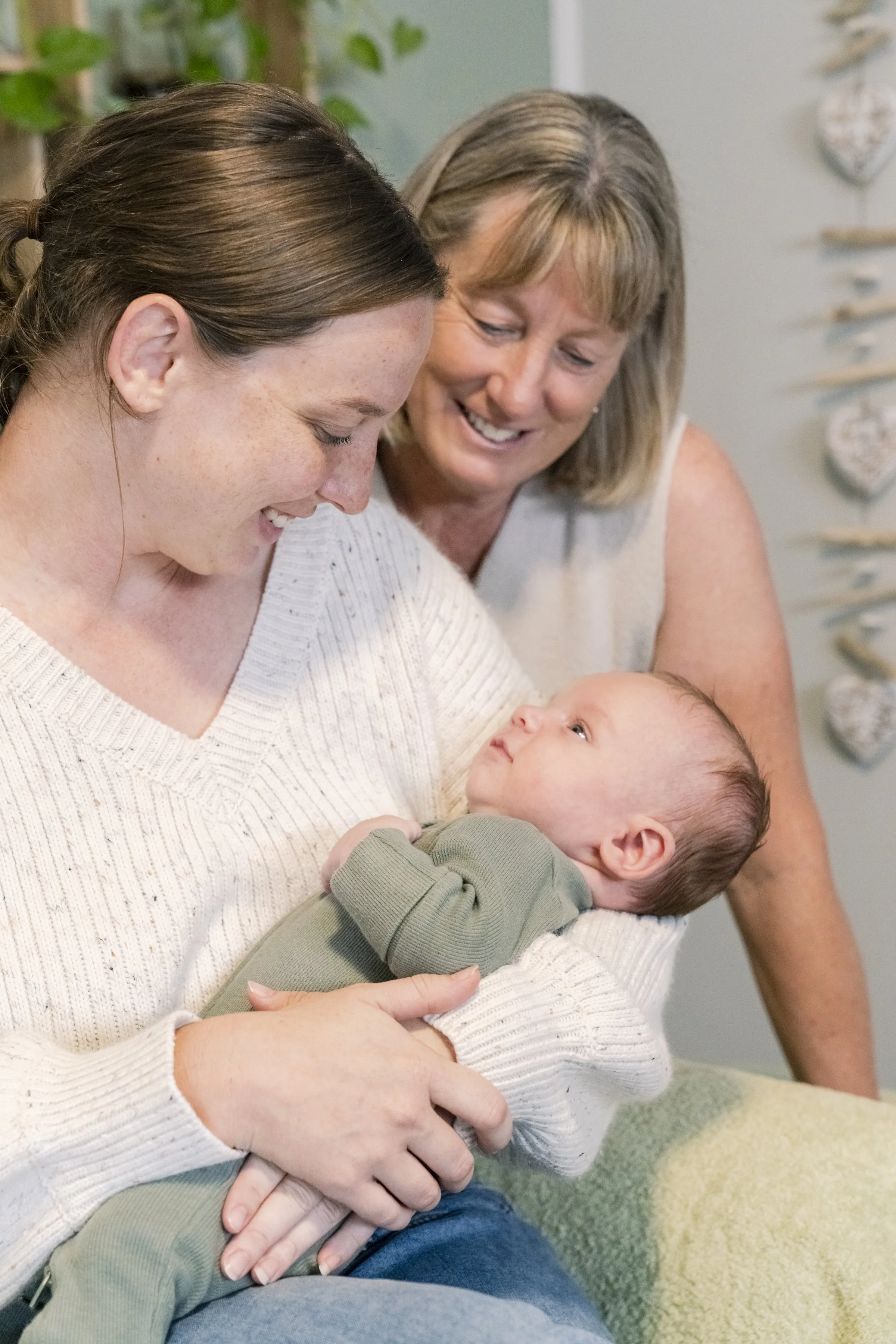 A woman holding a baby while another woman looks on smiling in the background.