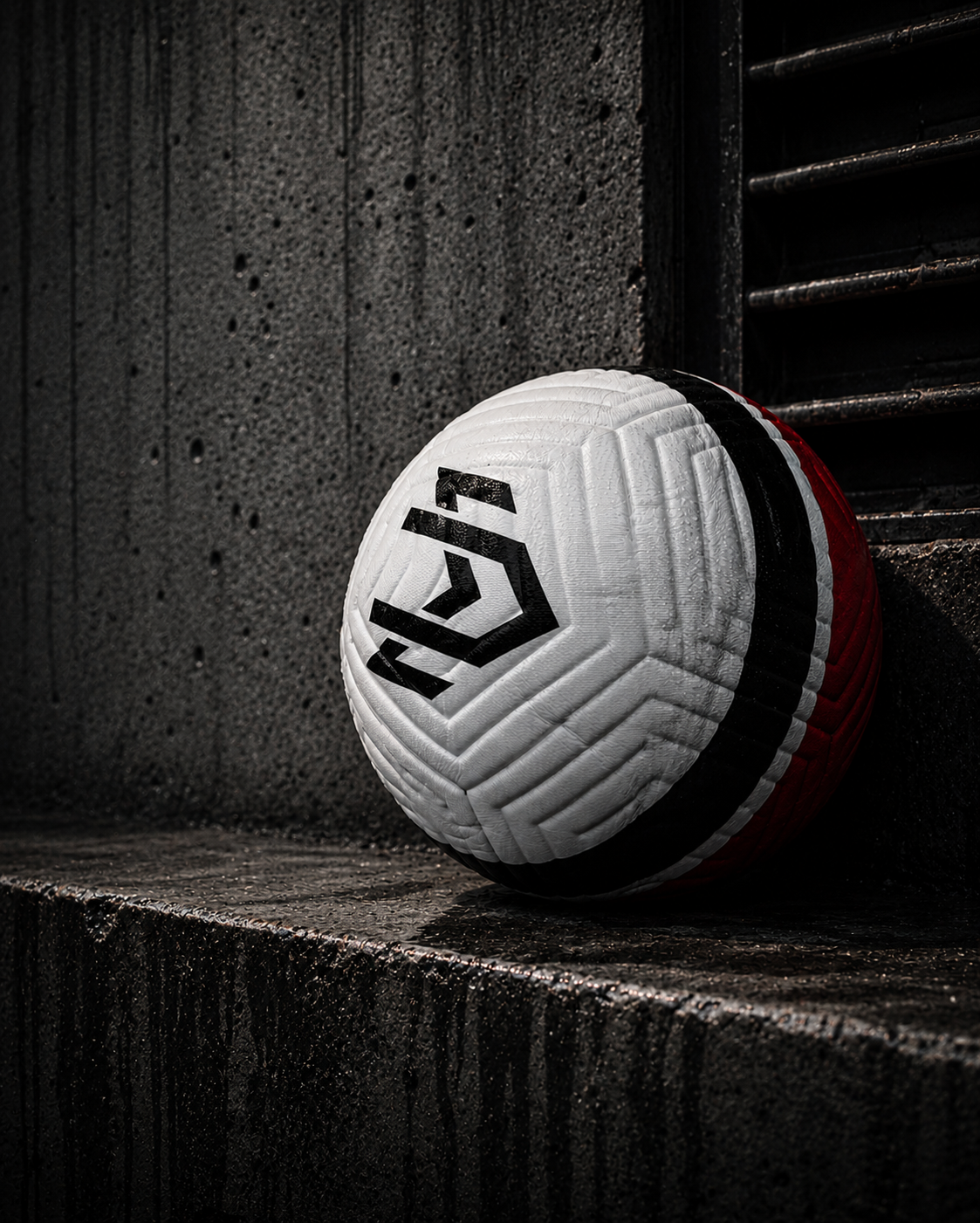 Europäische Handballmarke auf einem weißen, schwarzen und roten Handball, der auf einer dunklen, rutschigen Oberfläche neben einer Wand liegt.