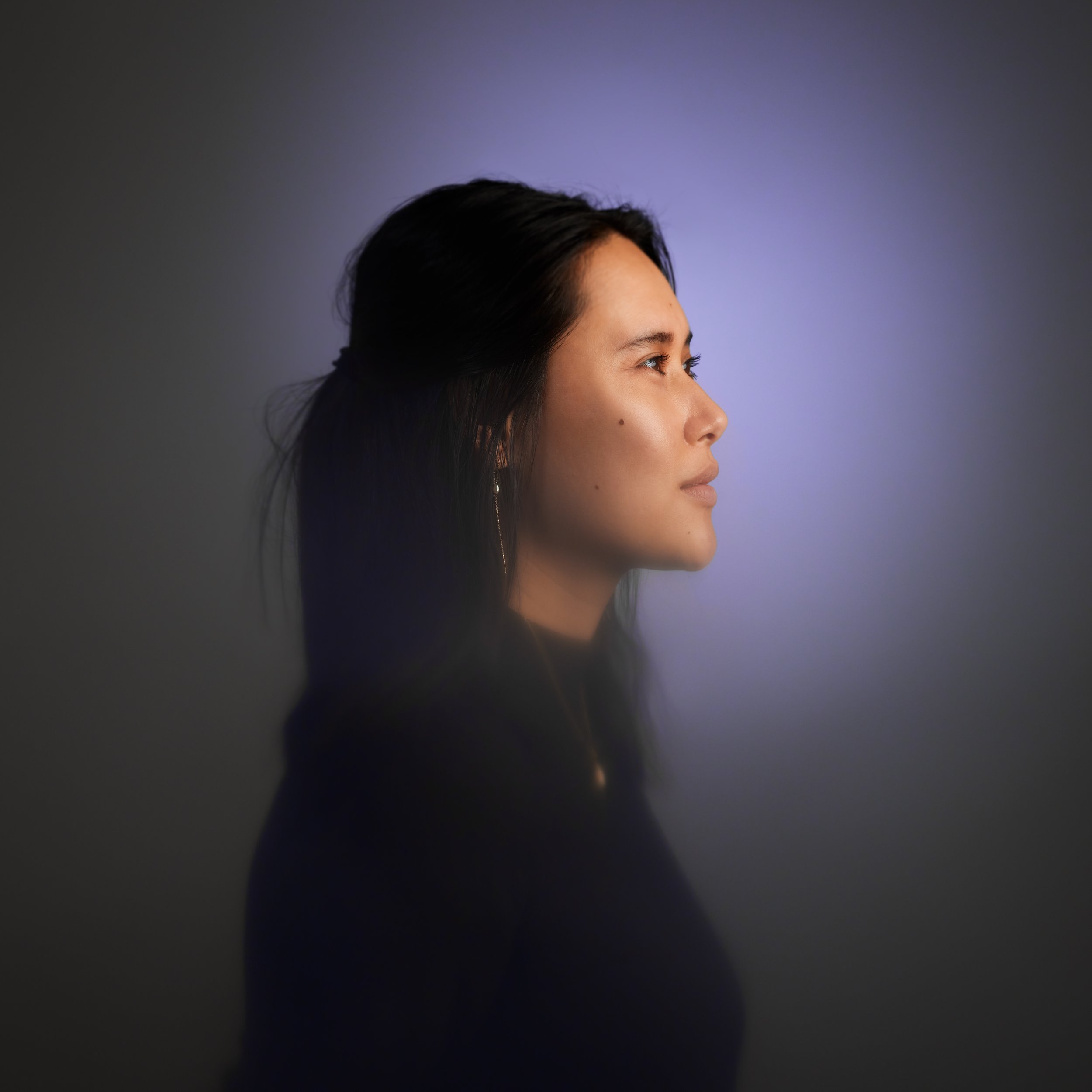 Profilbillede af en kvinde med mørkt hår, set i profil mod en blålig baggrund.
