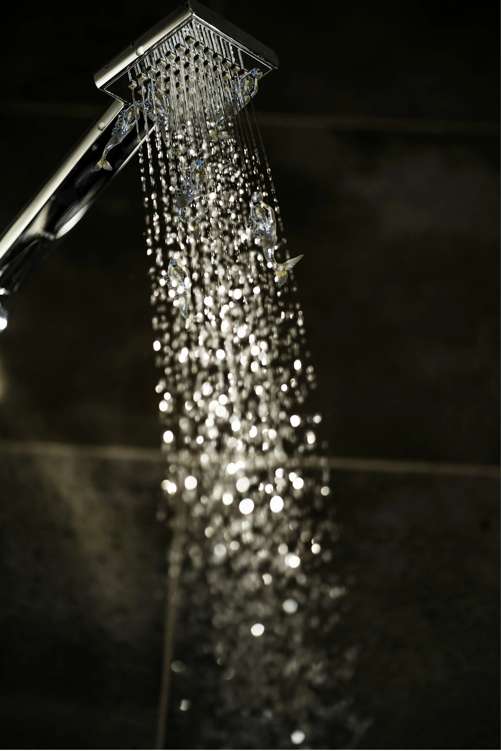 Showerhead with water and small fish-shaped jewelry beads cascading from it in a dark setting.