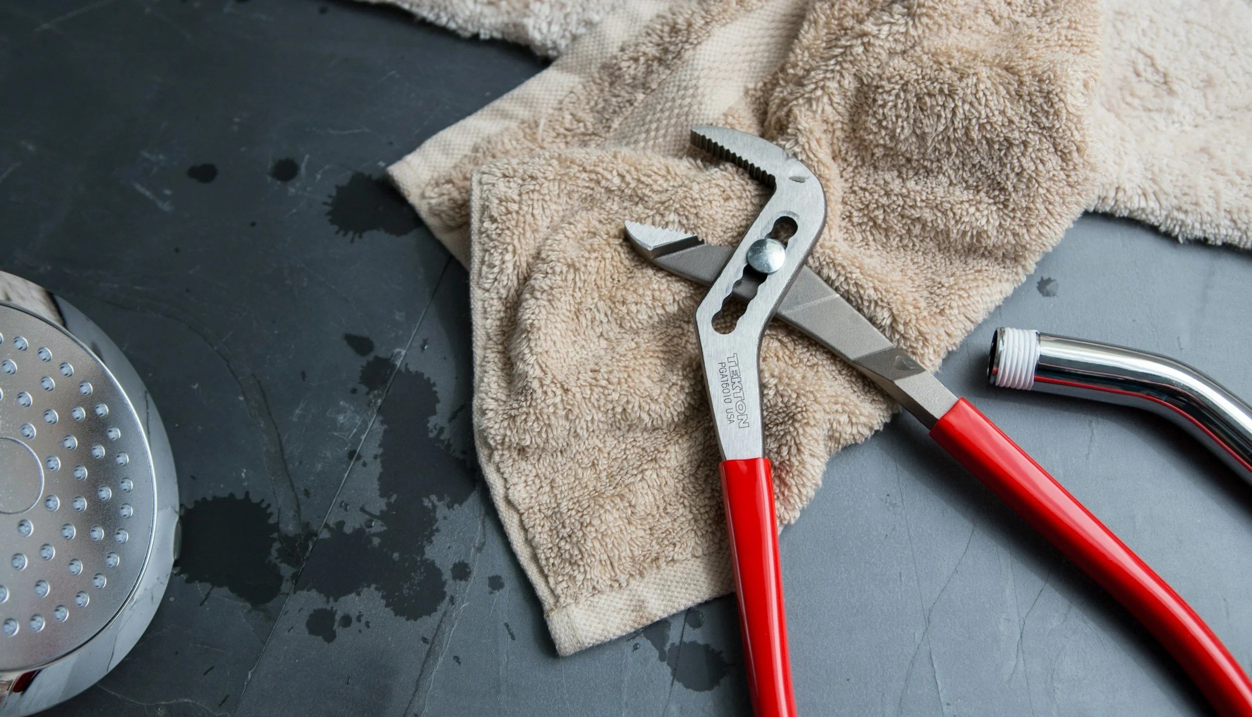 A hydraulic pipe cutter, a wrench, and a towel on a dark work surface with water stains.