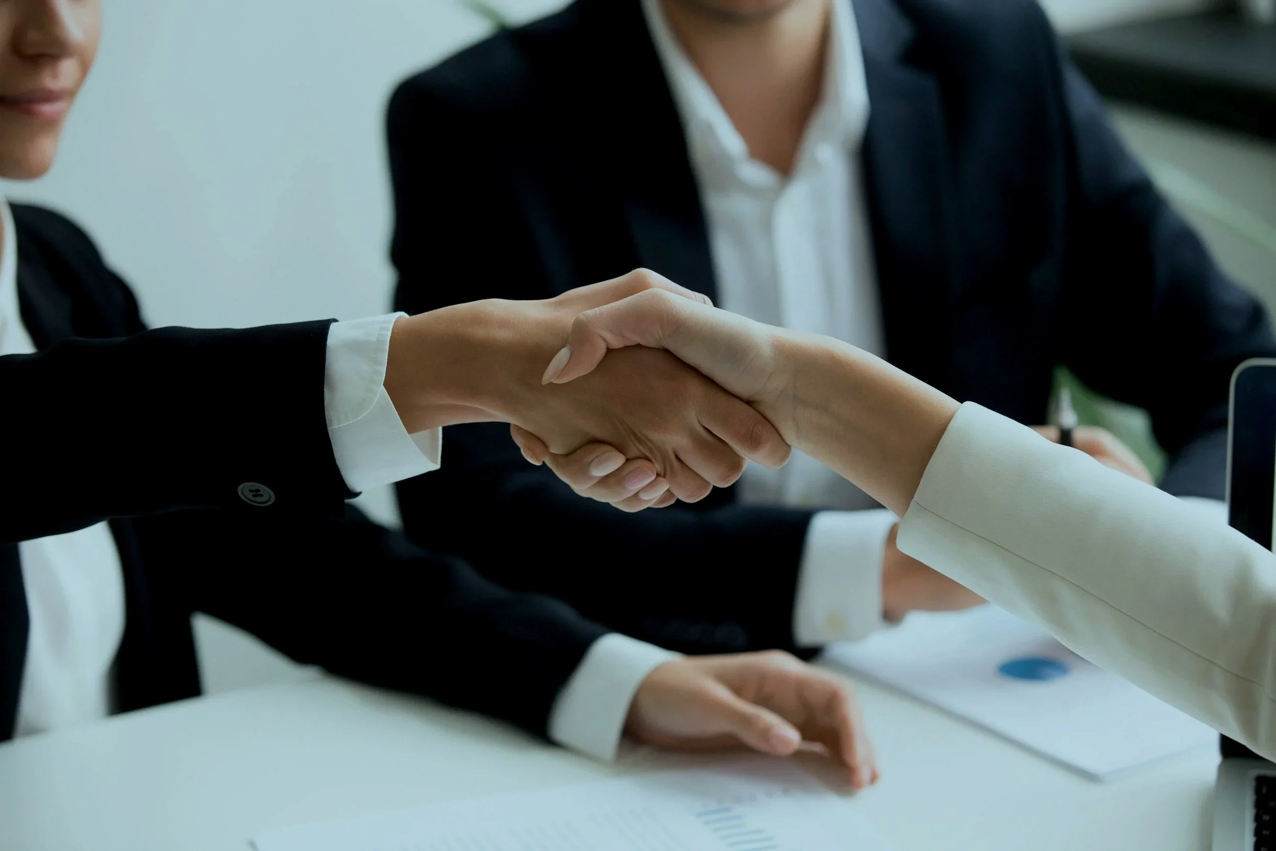 Two people shaking hands at a meeting table during a business discussion.