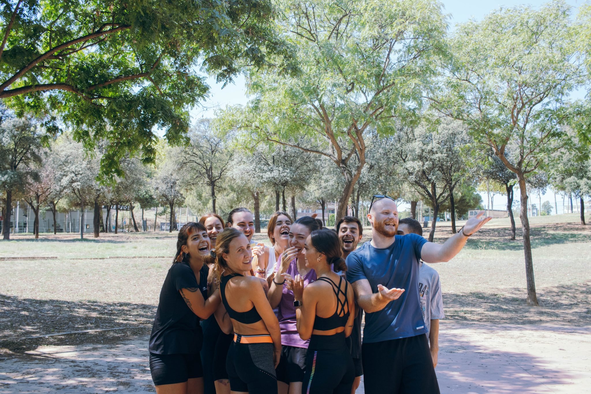 A group of happy people taking a selfie outdoors in a park with trees and clear sky in the background.