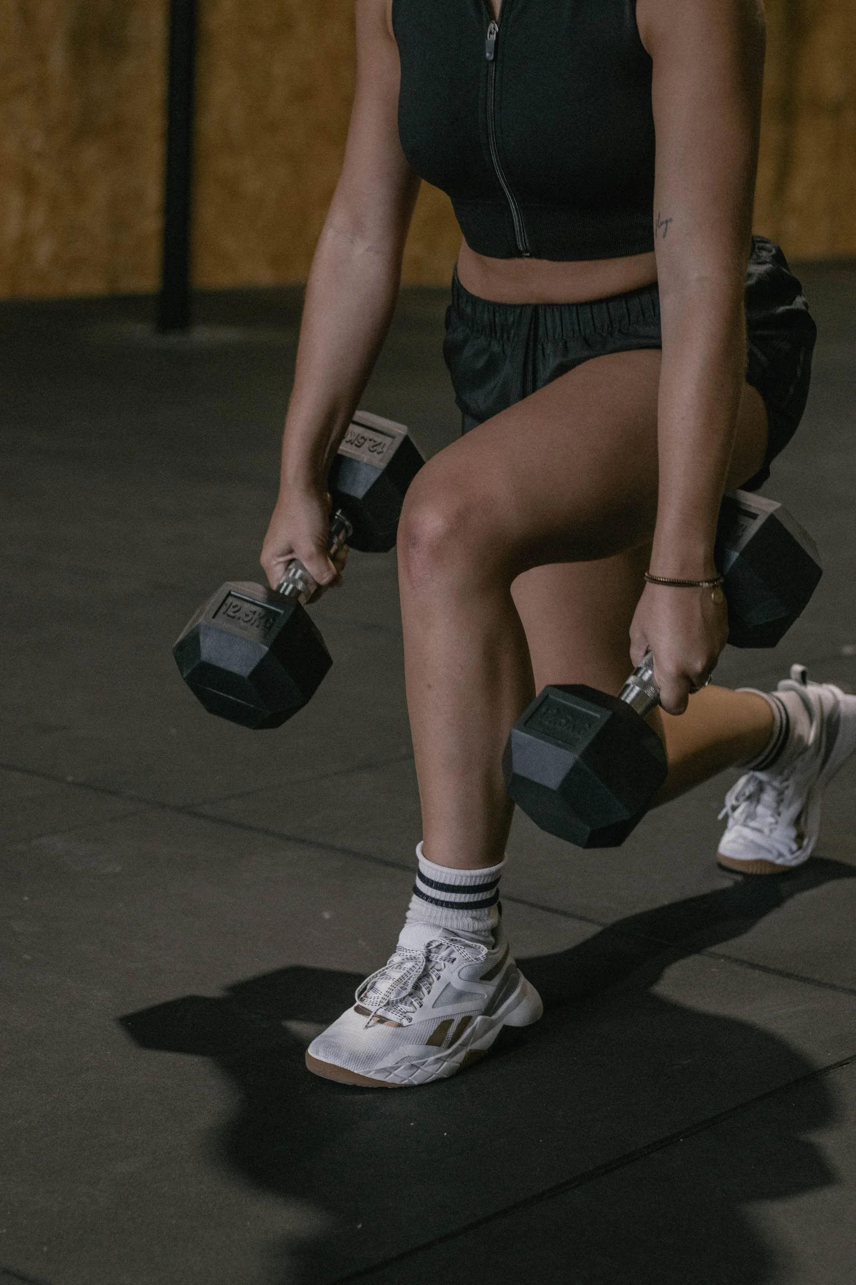 Person in athletic clothing lifting dumbbells during workout in a gym.
