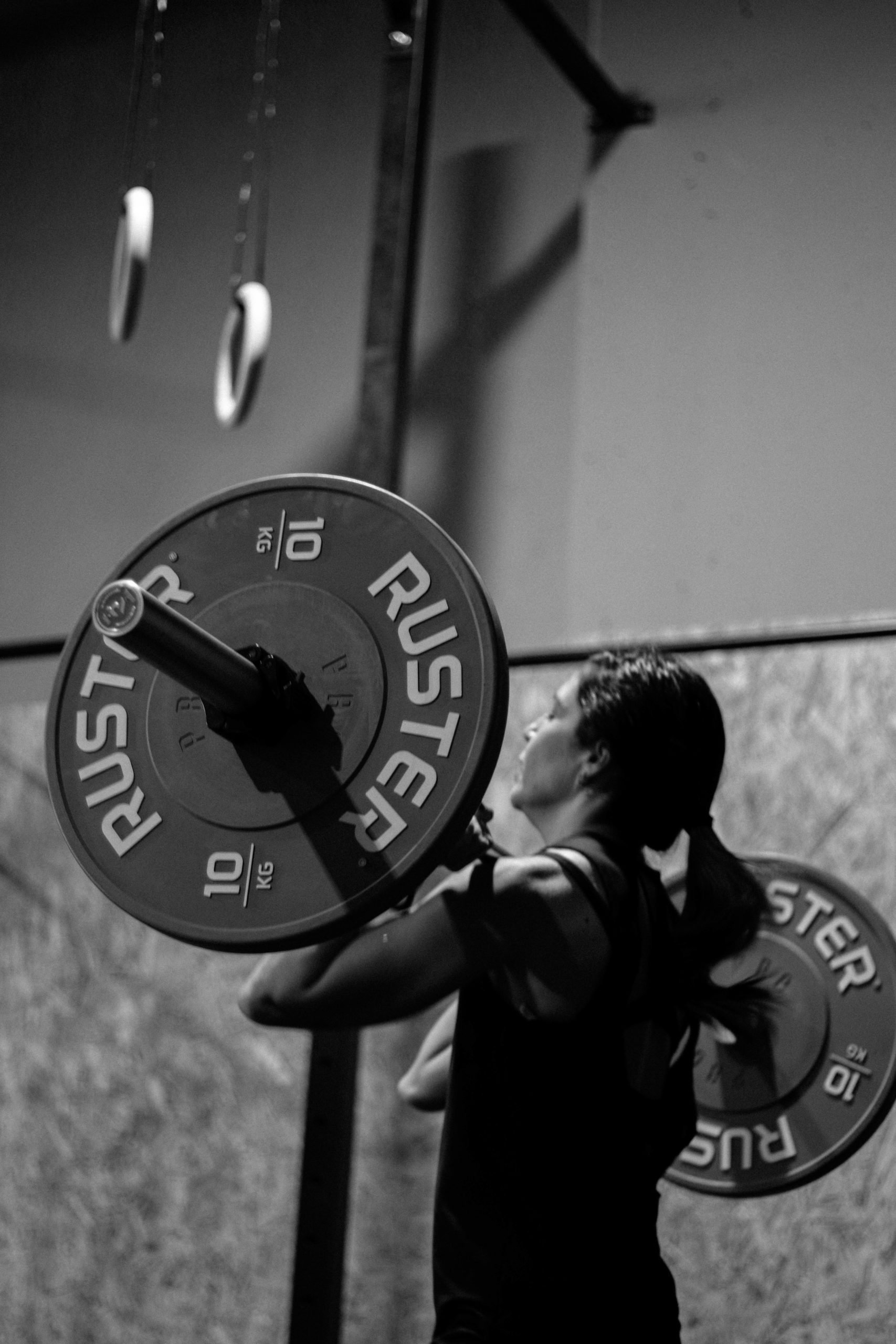 A person lifting a large weight plate in a gym, with gym equipment hanging from the ceiling.