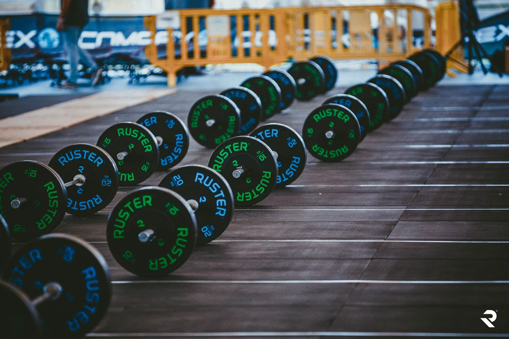 Row of black and green Ruster branded weight plates attached to barbells on a wooden gym floor.