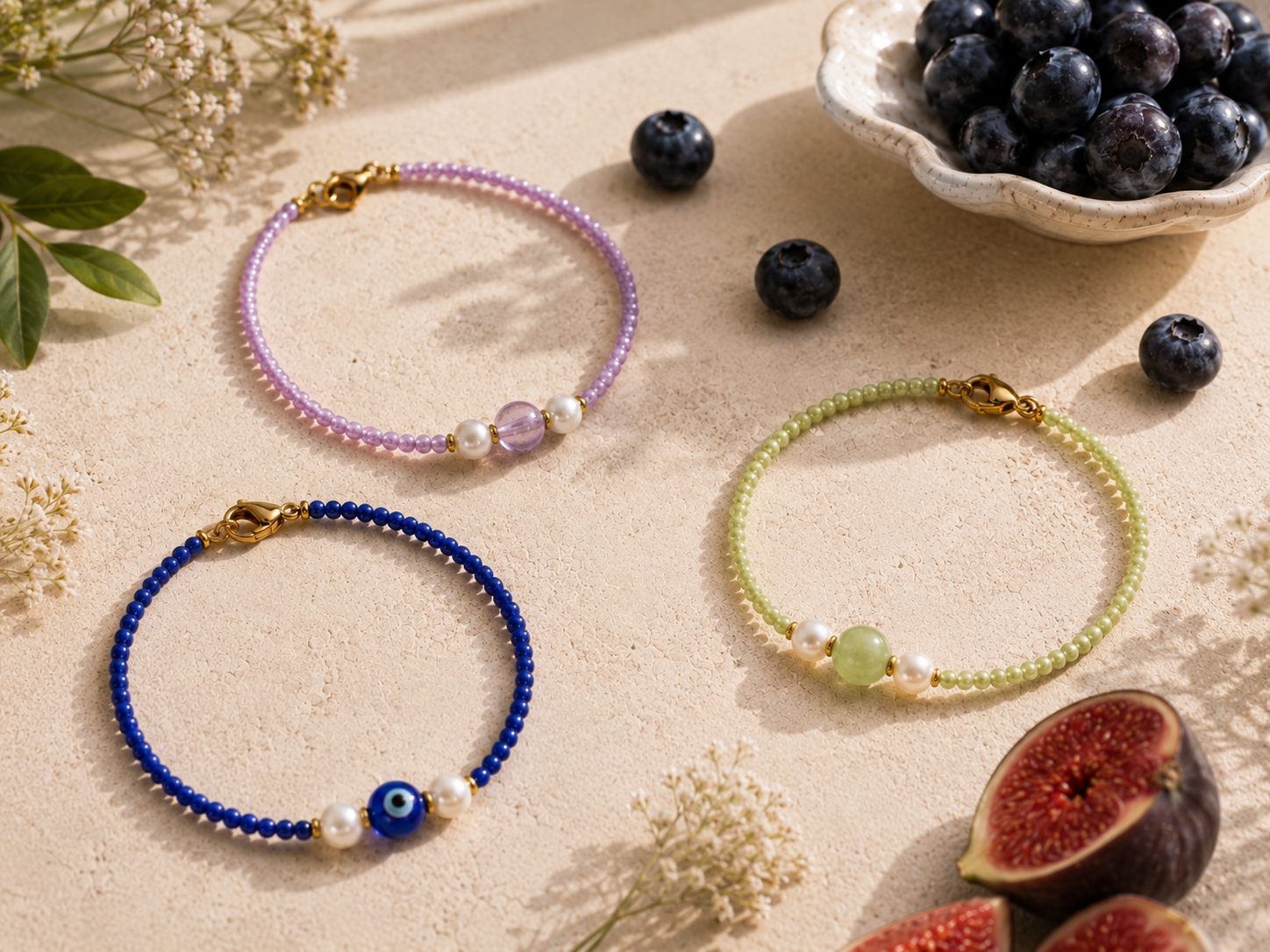 Summer Beaded Bracelets with Evil Eye and Gemstone Charms. Flat lay of four handmade beaded bracelets in green, lilac and navy blue with pearl details, gemstone centre beads, an evil eye charm and gold clasps.
