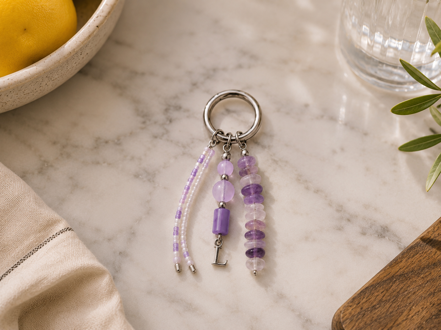 Pastel Lilac Beaded Keyring with Silver Initial Charm. Pastel lilac and pearl beaded keyring with silver hardware, layered purple gemstone-style beads, a silver initial charm and soft lifestyle styling.