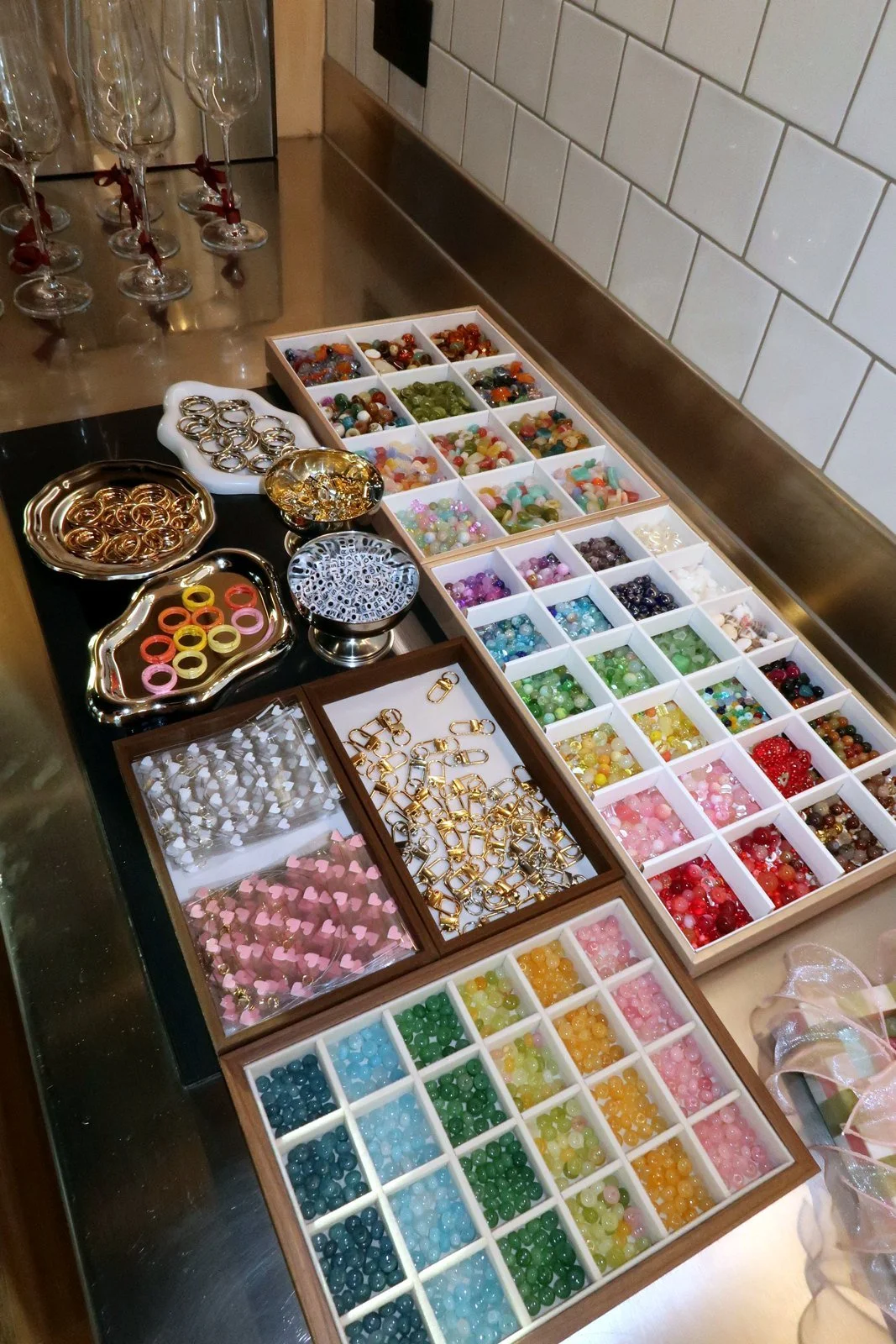 Trays of glass seed beads, freshwater pearls, gemstones and gold findings laid out for a Petals & Pearls jewellery workshop.