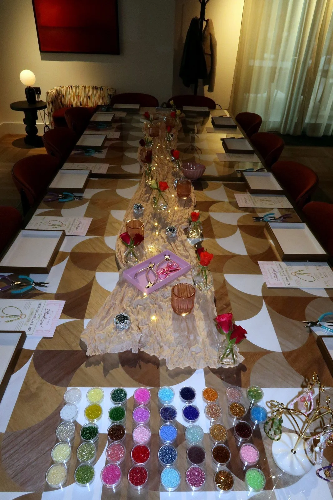 Jewellery-making workshop set up for a residents' evening at Vertus, Canary Wharf. Place settings, bead pots and fresh flowers down a long table.