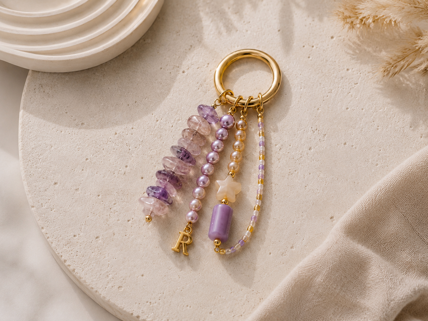 Pastel Lilac Beaded Keyring with Silver Charm | Petals & Pearls. Lilac and pink beaded keyring with gold hardware, purple gemstone-style beads, pearl-effect beads, a white star charm and gold initial charm on a soft neutral surface.