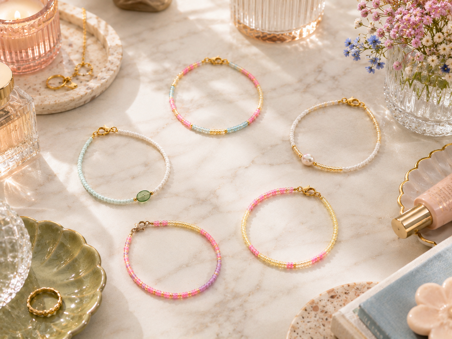 Five handmade pastel seed bead bracelets on a light marble vanity, featuring pearl details, gold clasps, colourful beads, soft flowers, candlelight and elegant lifestyle styling.