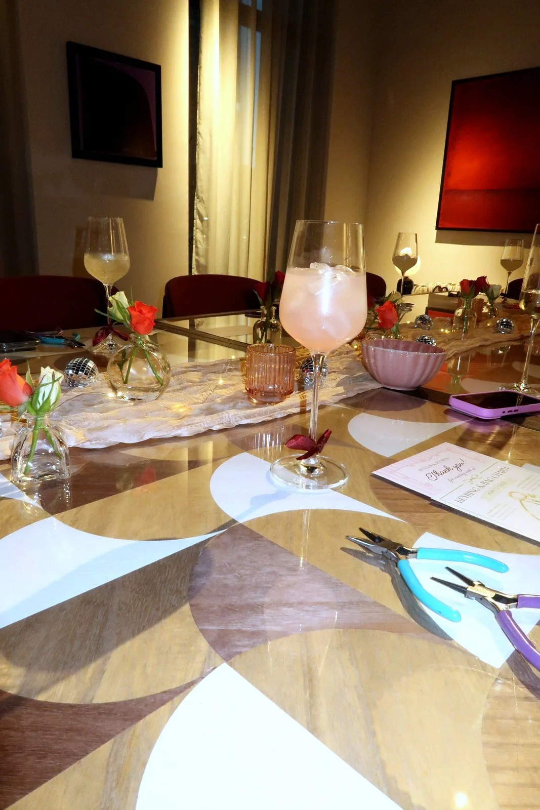 A guest's place setting at a Petals & Pearls workshop, with a drink, fresh flowers and jewellery pliers ready to use.