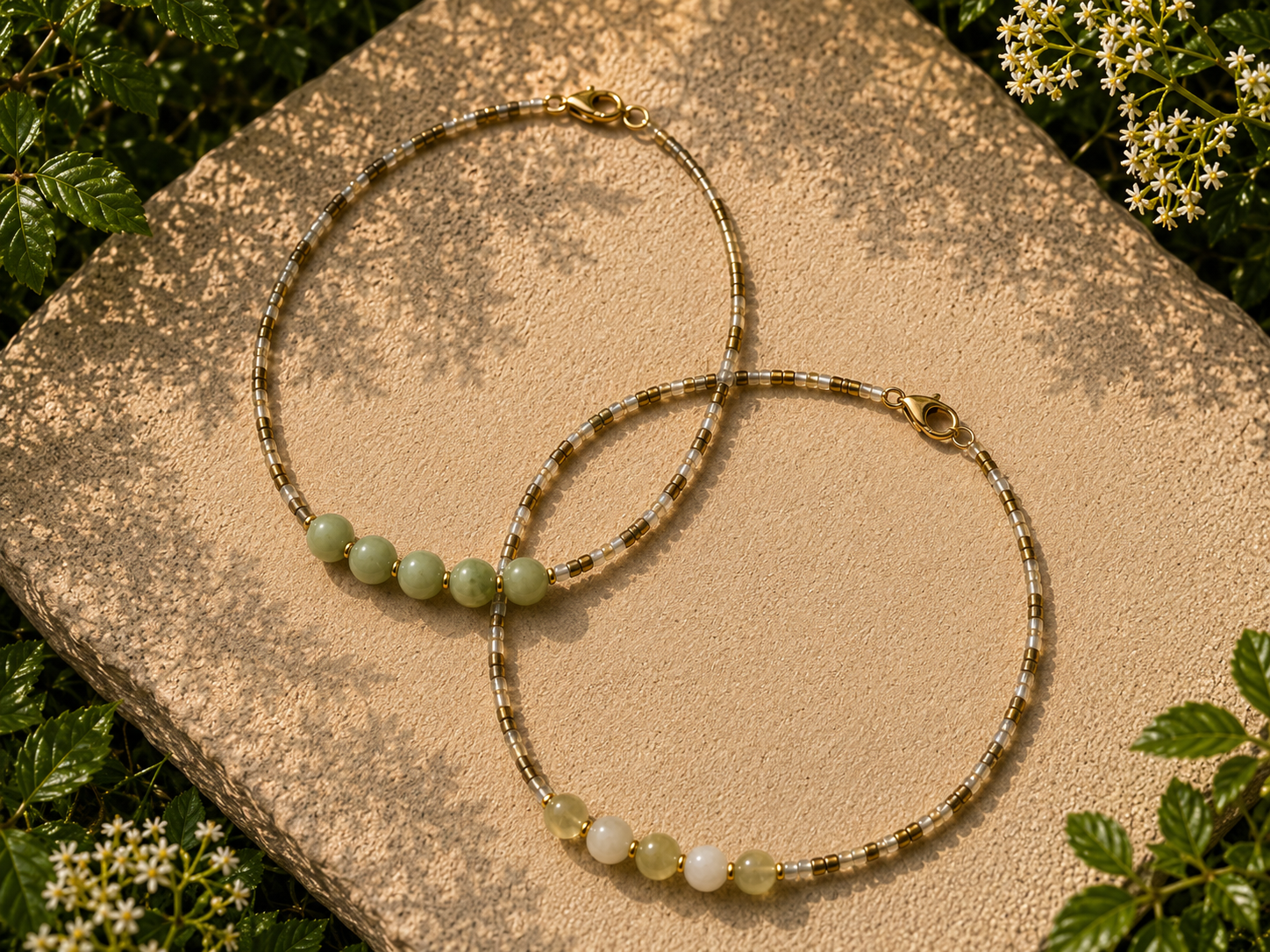 Earthy Green Beaded Necklaces with Jade Gemstone Beads. Two handmade earthy green seed bead necklaces on a sunlit stone surface, featuring pale green jade-style gemstone beads, gold accents and matching lobster clasp closures.