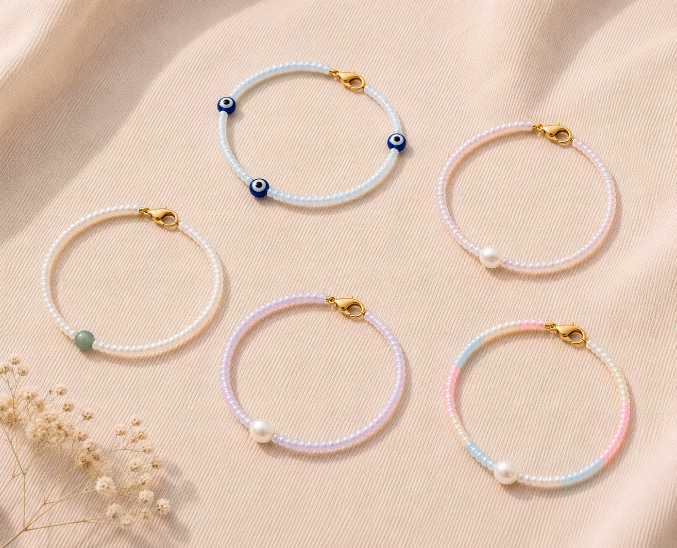 Pastel Beaded Bracelet Collection with Evil Eye Charms. Flat lay of five handmade pastel beaded bracelets with gold clasps, freshwater pearls, green accent beads and blue evil eye charms on soft beige fabric.