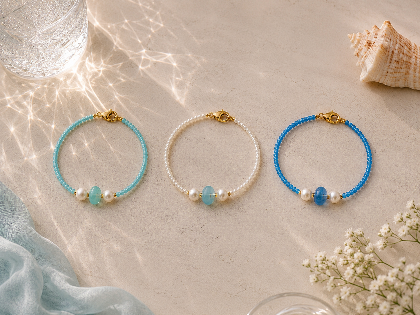 Ocean Gemstone Beaded Bracelet Collection | Petals & Pearls. Flat lay of handmade ocean-inspired bracelets in baby blue, turquoise and pearl white with gemstone centre beads, freshwater pearls and gold clasps styled with seashells and a starfish.