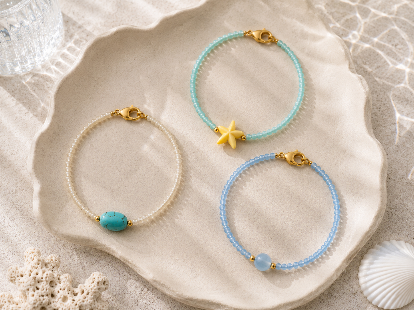 Seashell Inspired Beaded Bracelets with Starfish Charm | Petals & Pearls. Flat lay of handmade beach-inspired beaded bracelets in turquoise, pearl white and baby blue with gemstone centre beads, a yellow starfish charm and gold clasps on a shell-shap