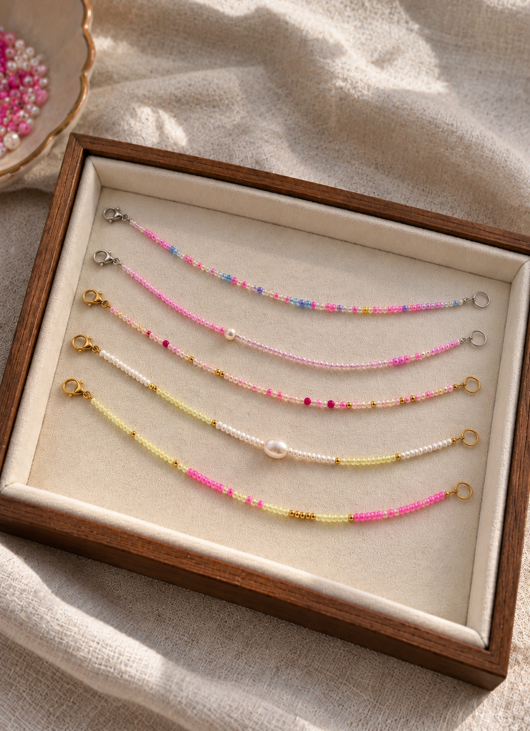 Pastel pink, yellow and white beaded bracelets with pearl and gold details displayed on a jewellery tray in natural sunlight.