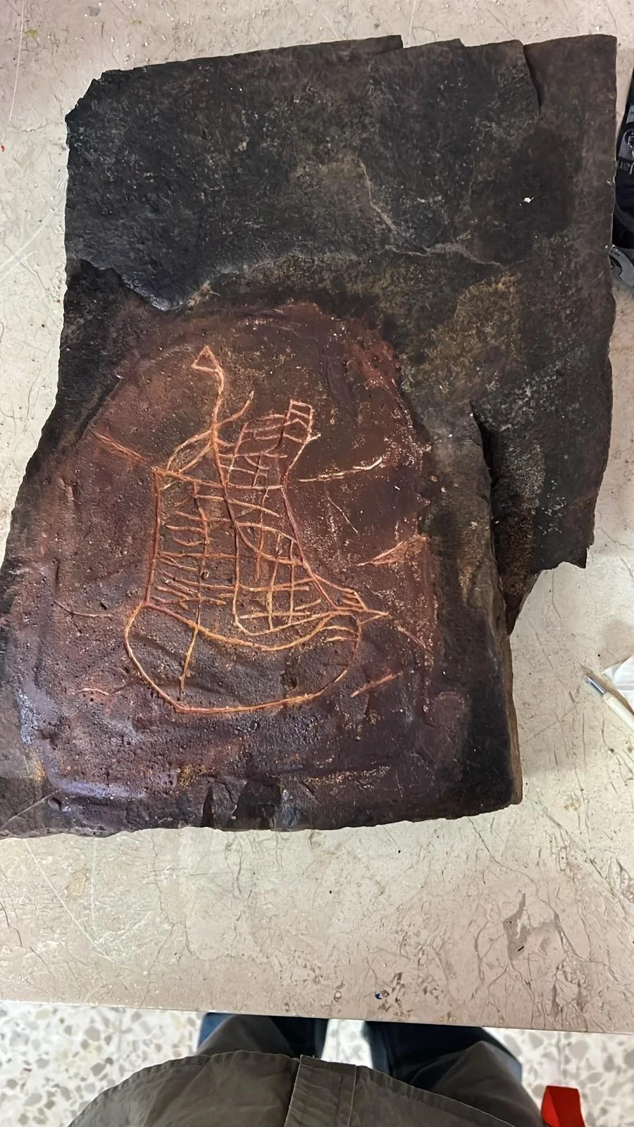 Lámina de piedra con grabado en forma de barco y red en su interior.