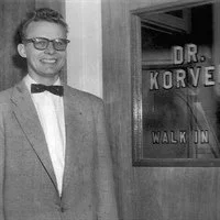 A man in a suit and bow tie standing next to a sign that reads 'Dr. Korve Walk In'.