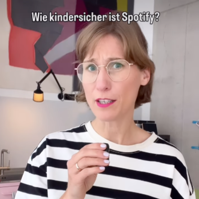 Eine Frau trägt eine schwarz-weiß gestreifte Bluse und spricht in einem hell erleuchteten Raum über Spotify, mit deutschen Texten im Video.