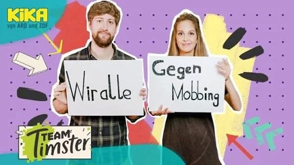 Ein Mann und eine Frau halten Schilder, auf denen steht "Wir alle gegen Mobbing". Im Hintergrund bunte, geometrische Formen und das Logo "KIKA" sowie "Team Limpster".