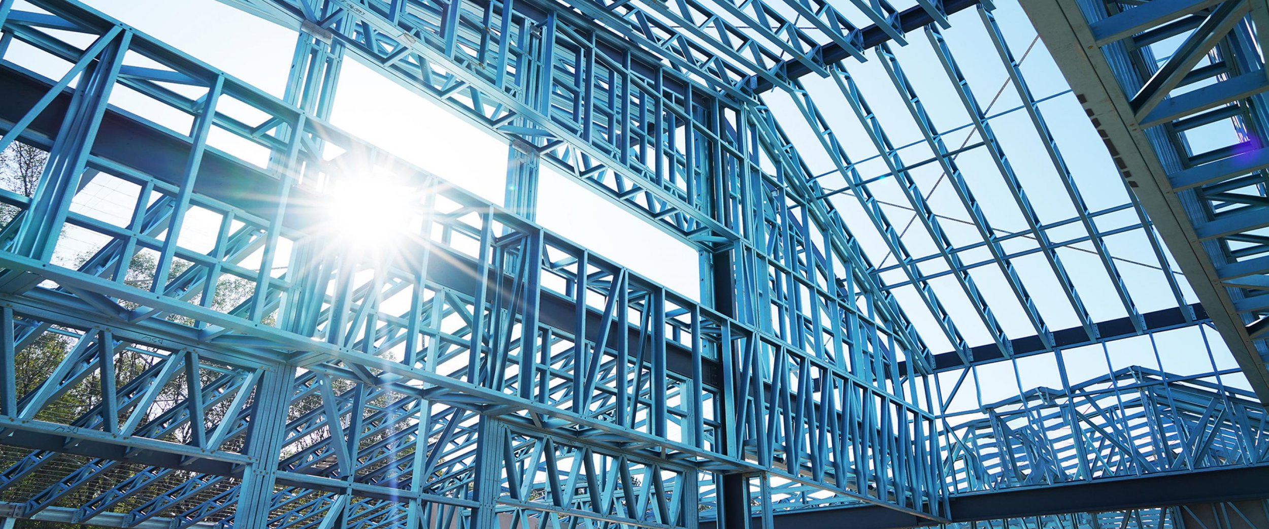 Blue steel framing structure of a building under construction with sunlight shining through.