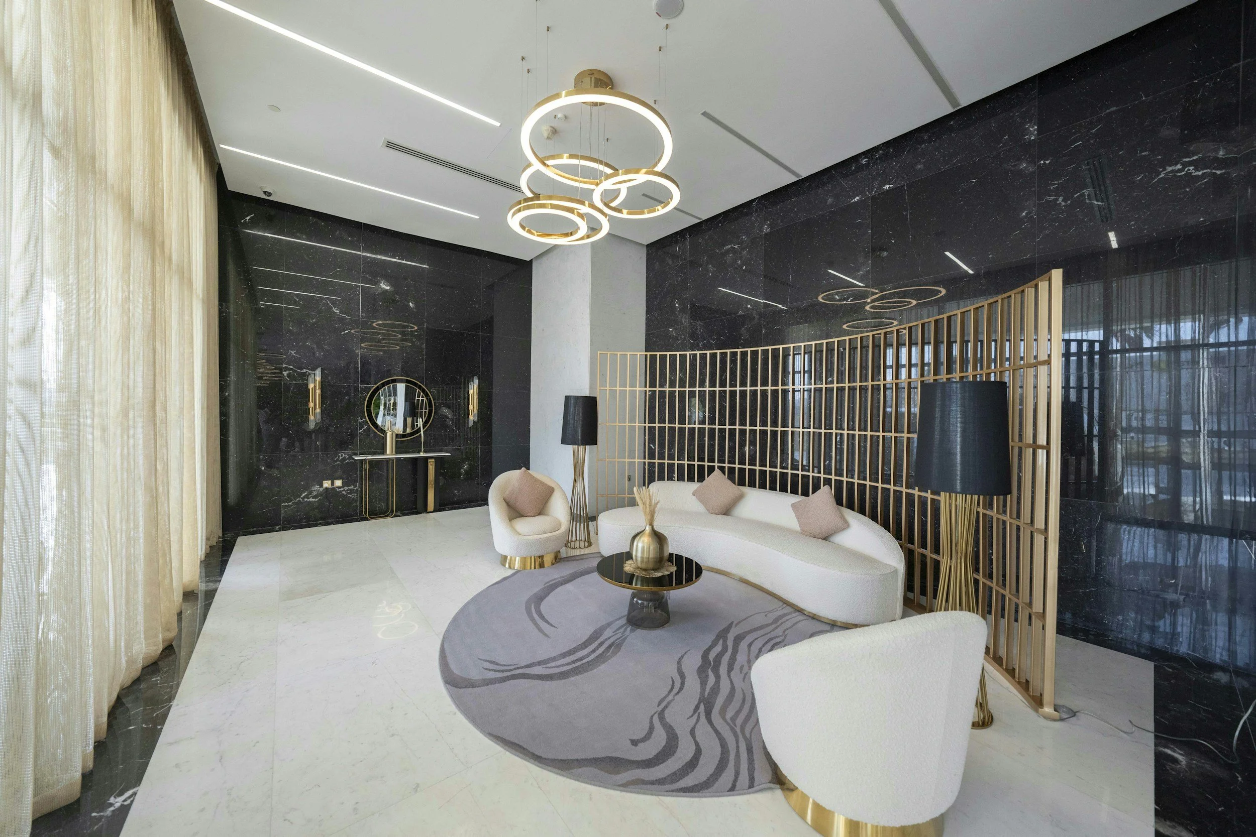 Modern interior living room with black marble walls, white curved sofa with beige pillows, gold and black accents, round area rug with abstract design, gold and black coffee table, black floor lamps, decorative screen, and contemporary circular ceiling lights.