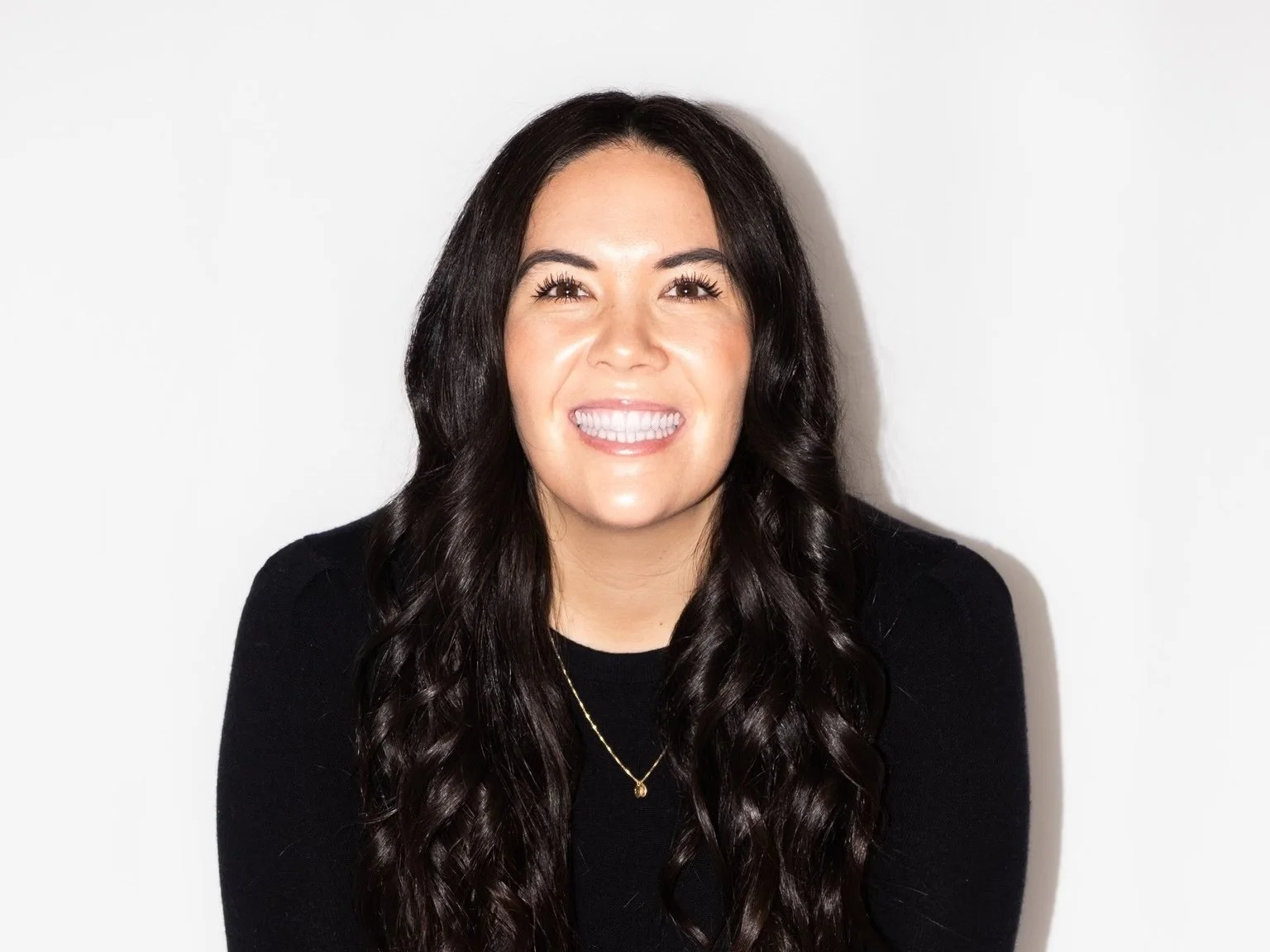 Portrait of a woman with long dark hair smiling against a white background.
