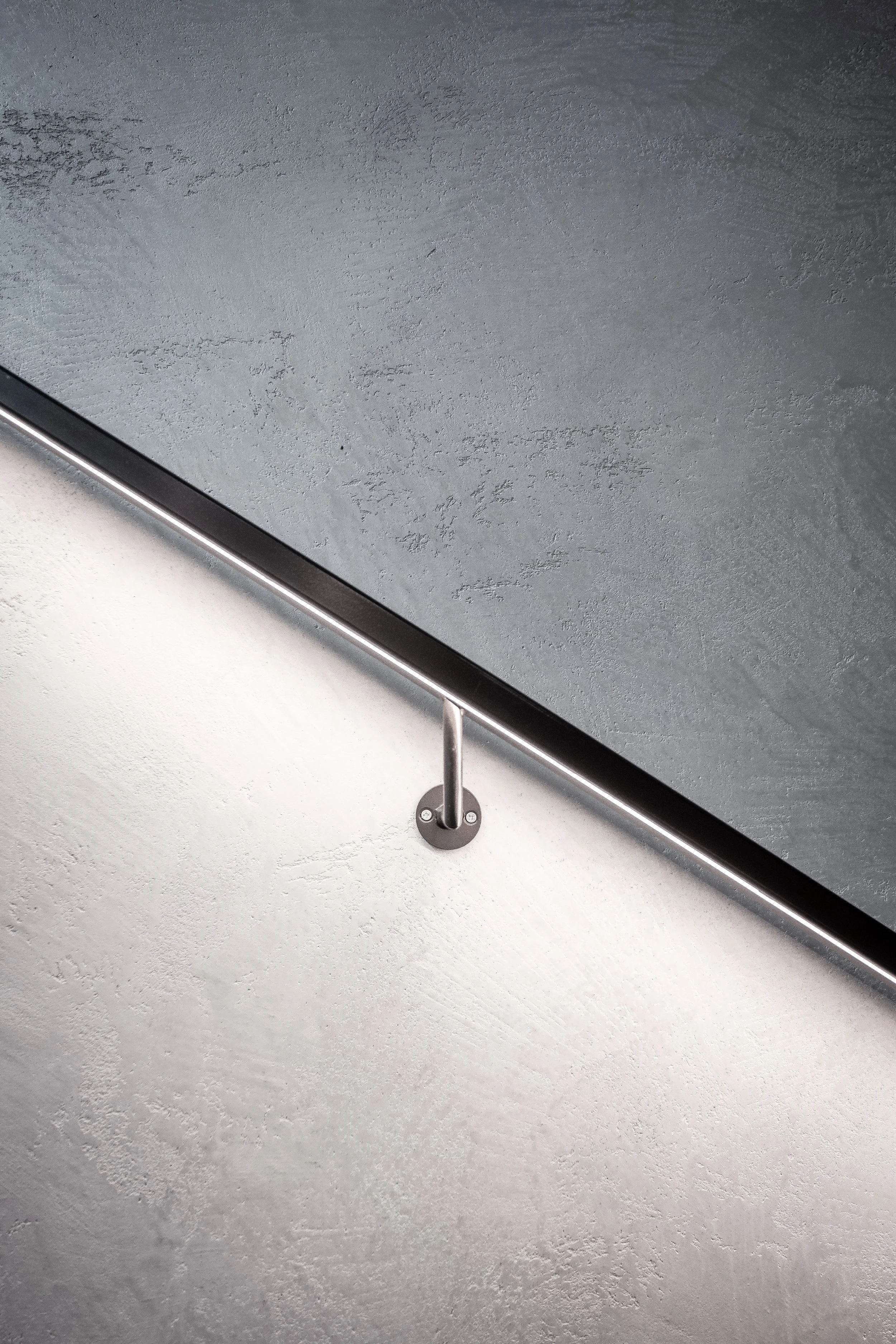 A close-up view of a section of a wall with a textured gray surface, partially showing a black flat screen monitor mounted on a wall bracket with a thin metallic border.