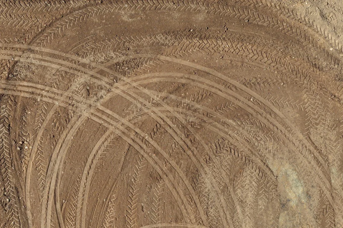 Close-up of a dusty, tire-tracked dirt surface with overlapping tire marks and treads.