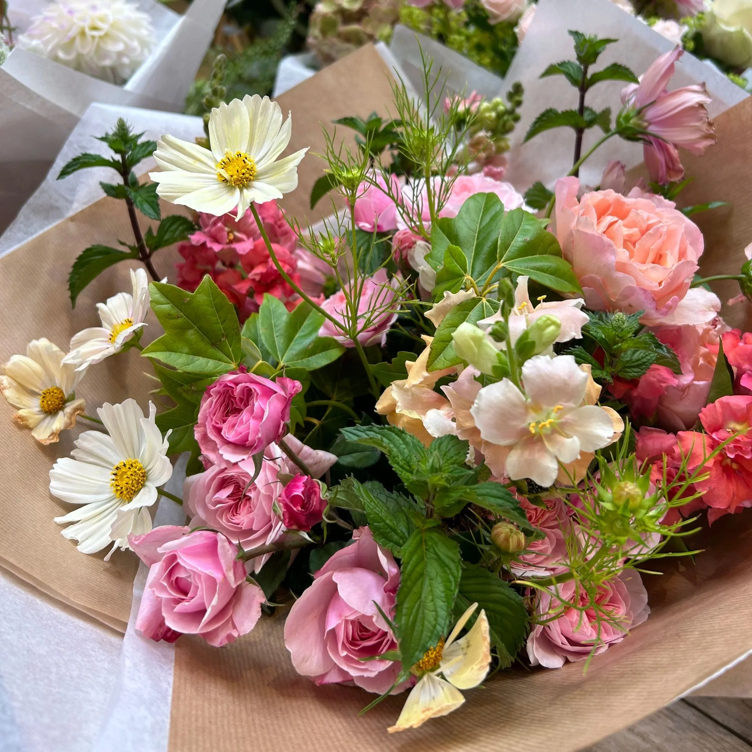 A bouquet of various pink and white flowers wrapped in brown paper and white tissue paper.