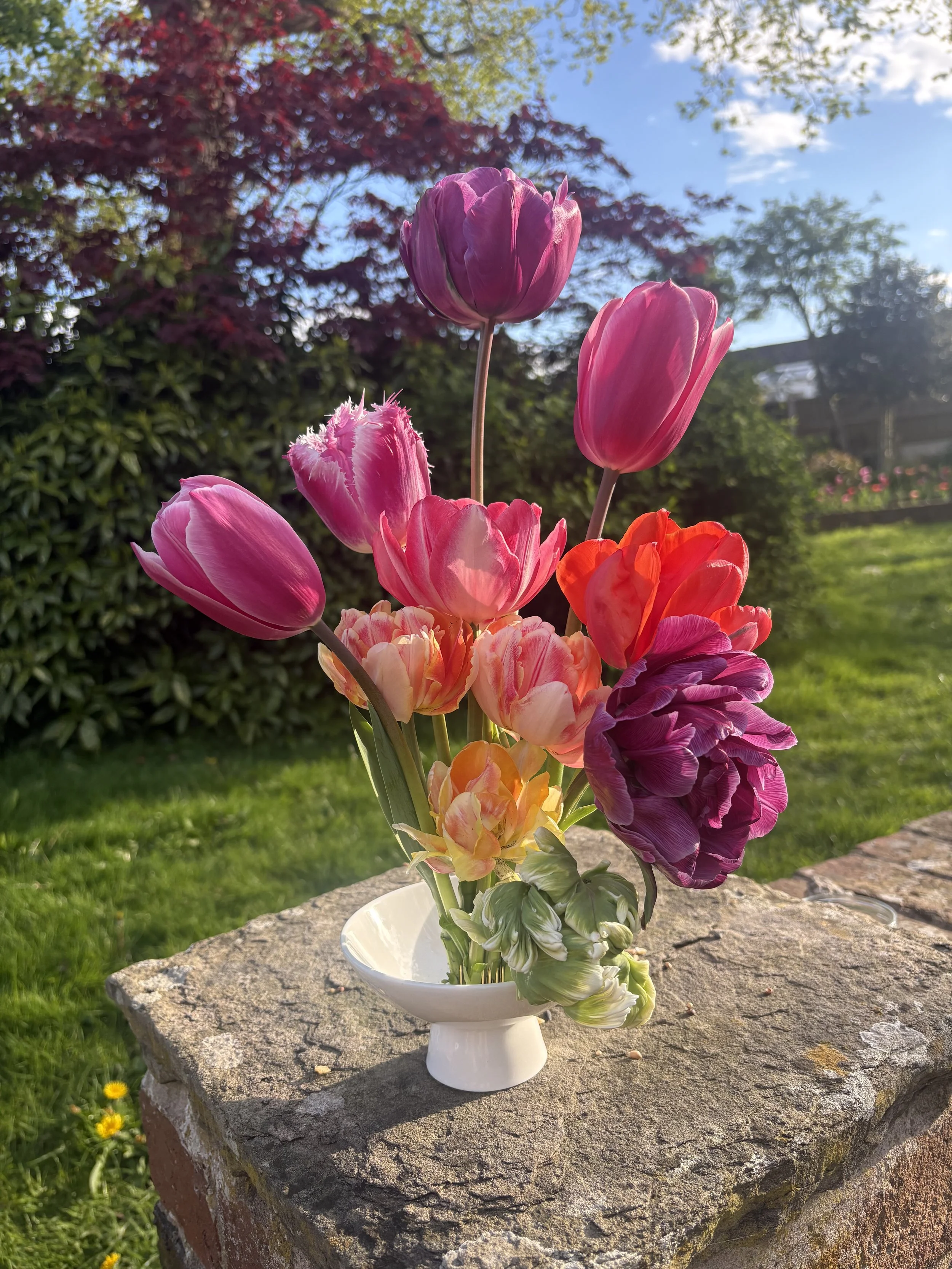 An arrangement of pink, purple, and orange tulips in a white vessel.