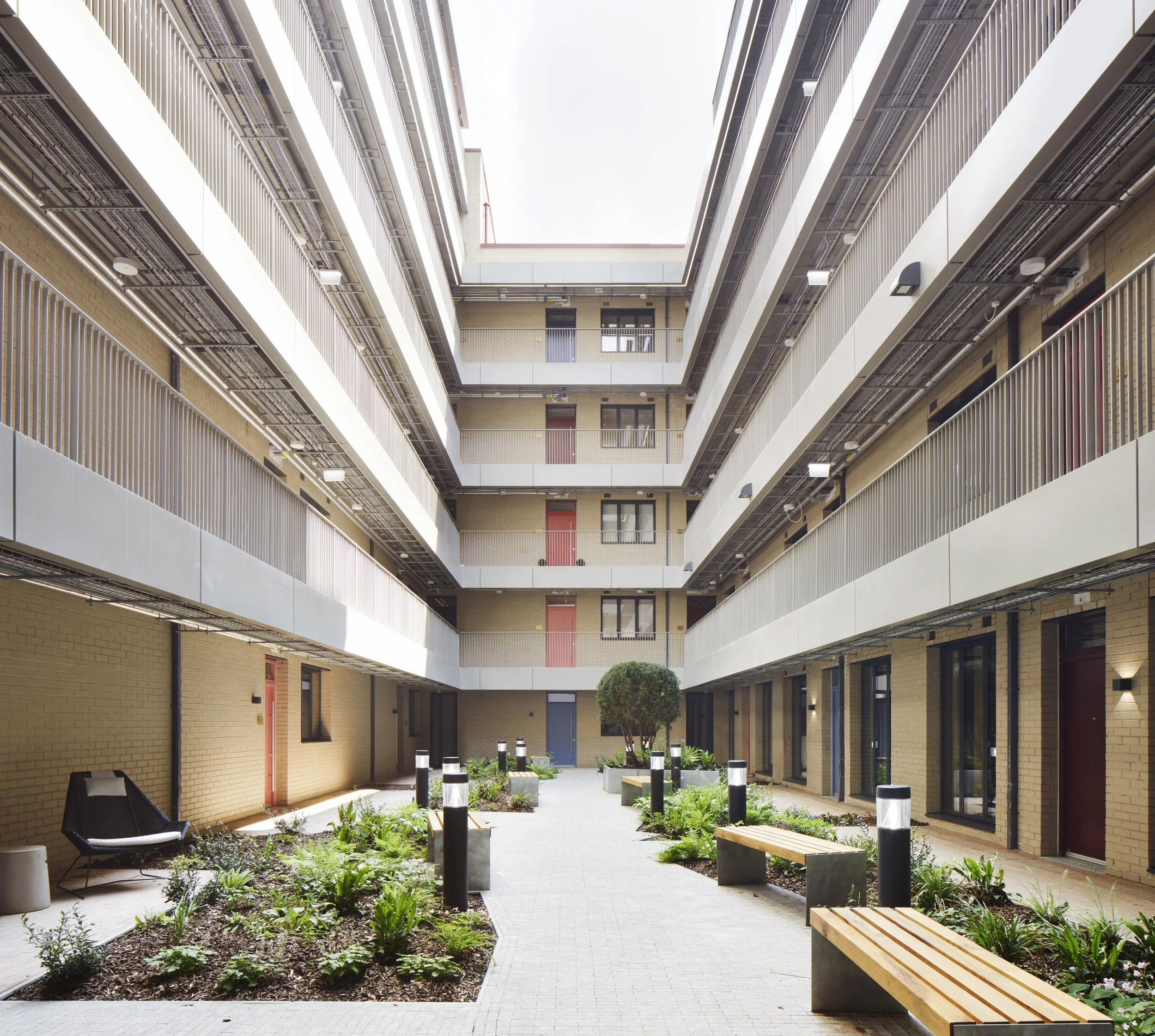 Interior courtyard of a modern apartment complex, New Cross Central, with multiple floors, brick walls, balconies, and a landscaped garden area with benches, plants, and pathway.